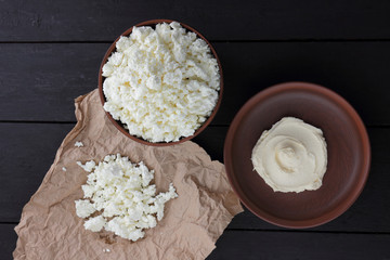 Cheese, fresh cottage cheese and sour cream in earthenware, goat curd on parchment paper, dairy products on a wooden background in rustic style, healthy food, copy space, dark background
