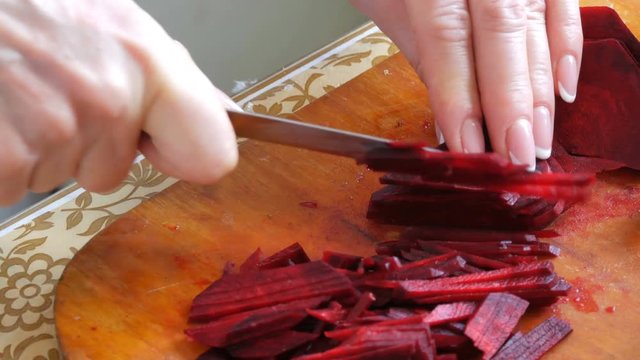 Female hands cut the beetroot on a kitchen board with knife