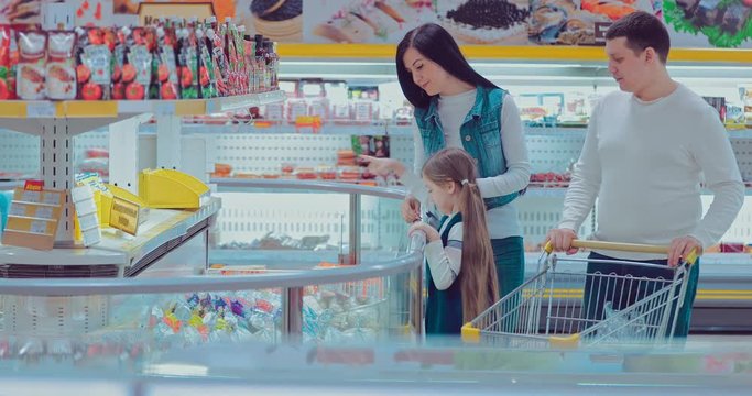 Young couple and children in frozen section. Woman taking prepack from the fridge