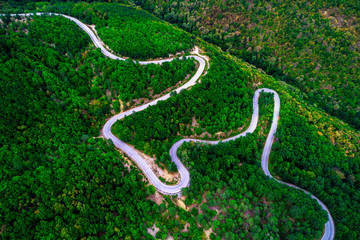 Aerial view  over mountain road and curves going through forest landscape