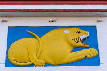 Madikeri, India - October 31, 2013: Shree Omkareshwara Temple. Mural of yellow lying male lion on white extermal wall. Set in sky-blue square under marron roof edge.