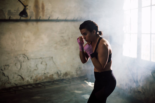 Strong brunette woman boxing indoors.
