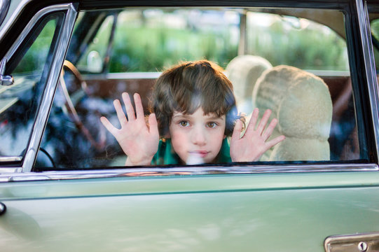 Boy sitting in car with hands on closed window