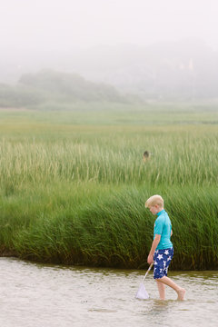 Per-teen boy fishing with a net in misty Cape Cod marshes