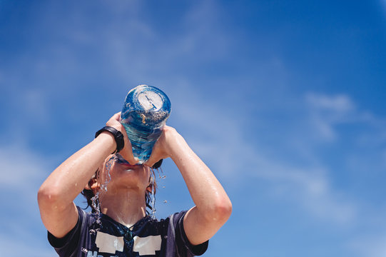 Boy drinking from a large water bottle at the beach in summer