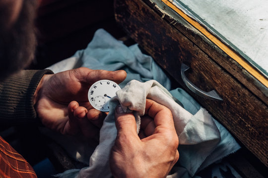 Watchmaker's hands cleaning a pocket watch dial
