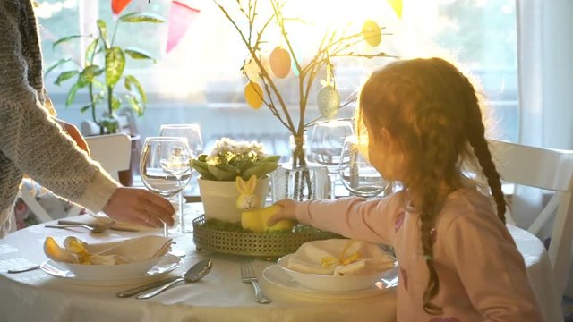 Young woman and her little daughter are setting easter festive table with bunny and eggs decoration. Slow Motion