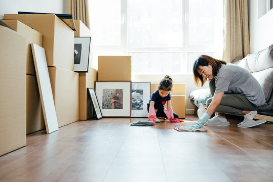 Adorable girl and her mother polishing wooden floor at new home