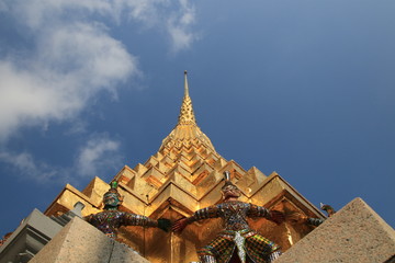 Fototapeta premium Close up colorful giant statues lifting the golden pagoda and white cloud blue sky in Wat Phra Kaew,Bangkok Thailand
