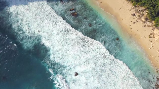 Aerial: Big Blue Waves Makes White Foam in Ocean near Sandy Beach. 4K. Nusa Penida, Bali, Indonesia.