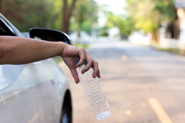 man's hand throwing plastic bottle out of car window, close up