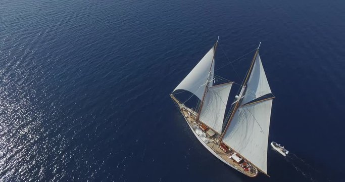 Epic drone shot flying above a luxury sailboat cruising on calm blue waters