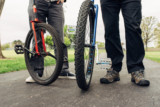 Low section of unicycle riders standing with unicycles on road