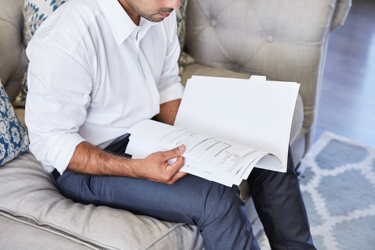 Hispanic businessman reading a contract in a folder at home on the sofa in living room