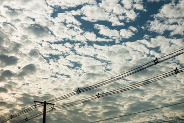 Fototapeta premium Sky full of fluffy cloud with sun light in daytime and with electricity powerling silhouette in foreground