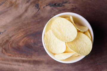 Potato chips in a bowl on wooden background, top view of food