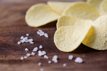 Potato chips and salt on wooden background