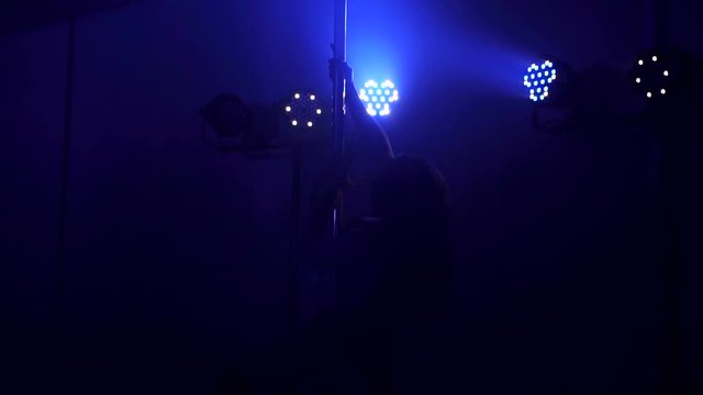 Young slim woman's silhouette dancing near the pole in dark room. Slow motion.