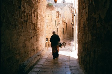Old woman is walking in a narrow way at old town Mdina.