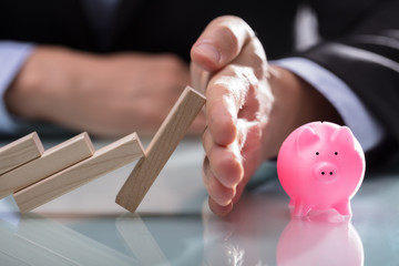 Businessman Stopping Wooden Blocks From Falling On Piggybank