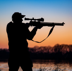 silhouette of hunter with rifle on the background of sunset. man with a gun against the evening sky...