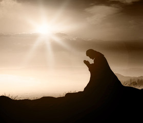 Miracle salvation concept: Silhouette Jesus Christ of Nazareth kneeling and praying at garden of...