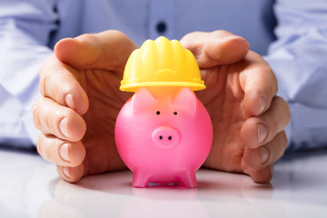 Person Protecting Hard Hat And Piggy Bank