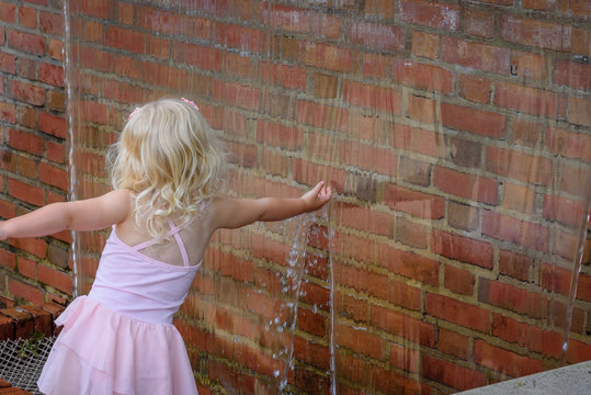 little girl reaching her hand into waterfall wall touching water
