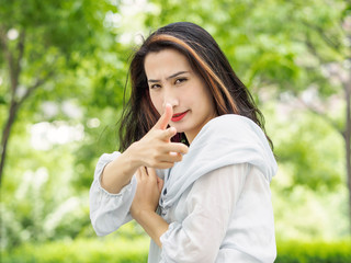 Beautiful young brunette Asian woman aiming at camera with hand gun gesture. Outdoor fashion portrait of glamour young Chinese stylish lady. Emotions, people, beauty and lifestyle concept.