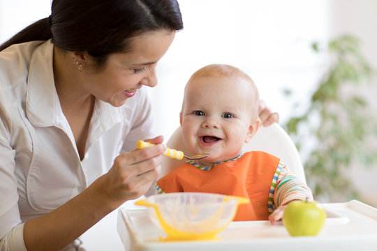 Mom giving homogenized food to her baby son on high chair.