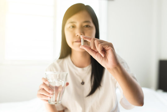 Young asian woman with pills or capsules on hand and a glass of water