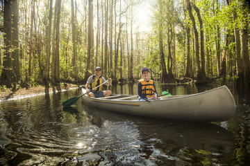 Adventuresome Father and son canoeing together on a beautiful river in a thick forest
