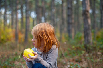 A girl in the forest holds an apple