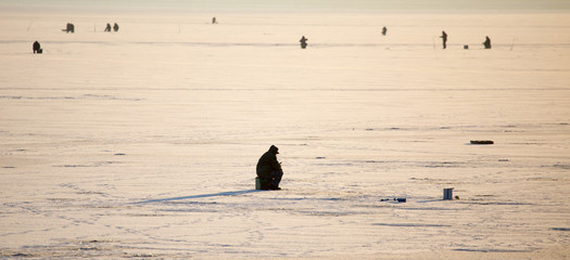 A man on ice is fishing in the evening