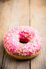 Donut with sprinkles on the rustic wooden background. Selective focus.