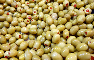 Pile of salted green olives stuffed with red pepper as background.