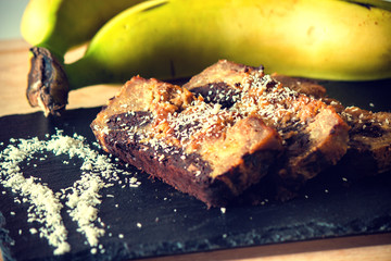 Banana and chocolate bread on a black plate with coconut and bananas in the background.