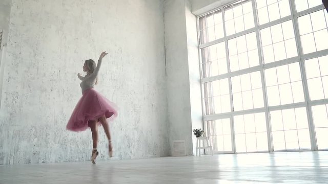 graceful young ballerina dancing against the backdrop of a huge light window. ballet dancer in a classic tutu and pointe