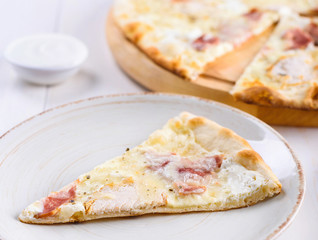 Slice of fresh cheese pizza with  ham and cream sauce on white plate, close up. Italian traditional cuisine, copy space. Food, shallow depth of field