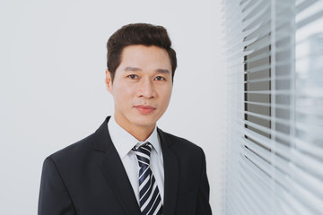 Smiling asian businesman standing by the window.