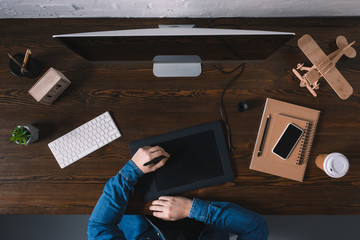 partial top view of person using graphics tablet while sitting at workplace