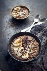 morning chocolate oat porridge with fresh bananas on black background