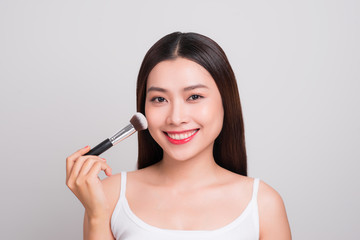 Beautiful young asian woman with perfect skin applying makeup with a brush