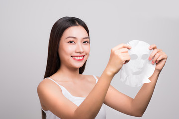 Beautiful asian woman applying paper sheet mask on her face white background.