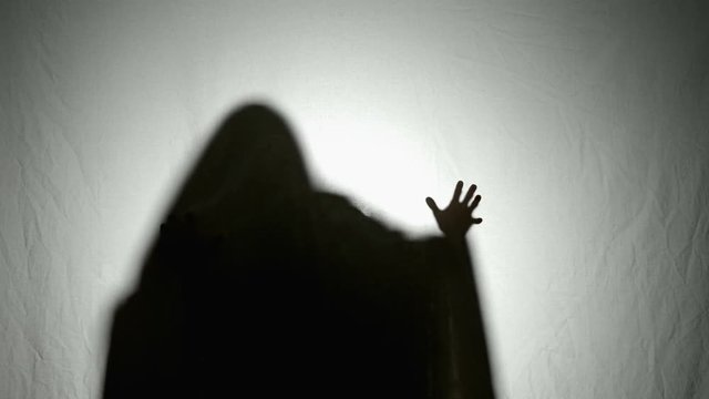 Shadow silhouette of a covered halloween ghost moving its hands in a scary frightening way