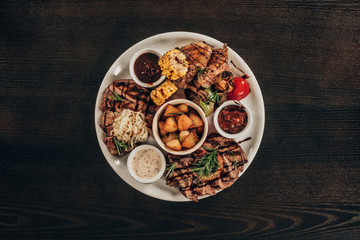 top view of plate with beef steaks, chicken wings and grilled vegetables on wooden table