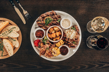 top view of plate with beef steaks, chicken wings and wine with bread on wooden table