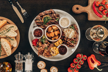 top view of plate with beef steaks, chicken wings and grilled vegetables on table