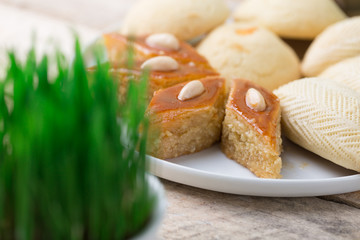 Traditional Azerbaijan Novruz table decoration setting for spring equinox new year celebration, white plate with shekerbura and pakhlava, various size wheat grass symbol Nowruz, close up copy space