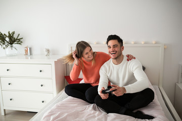 Fototapeta na wymiar Young couple sitting on bed playing video games laughing